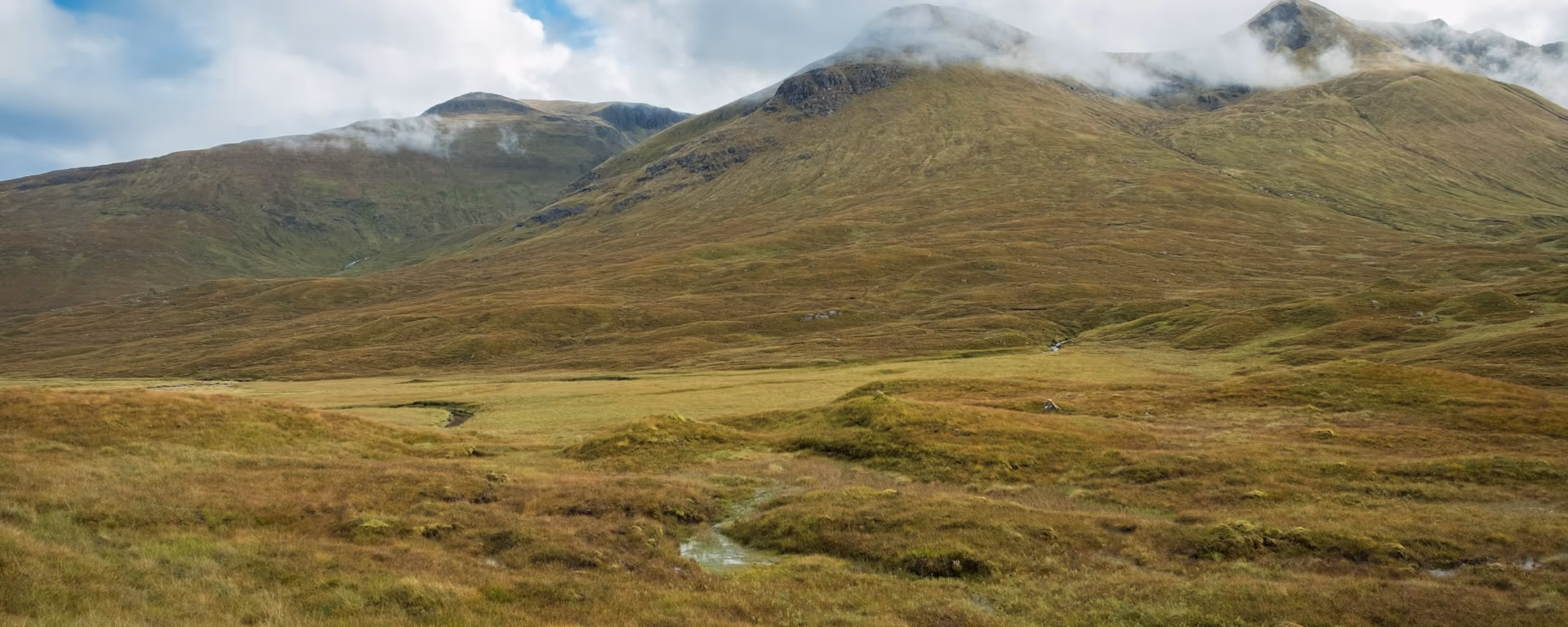 Tawny glen and a burn looking up to cloud-wrapped peaks