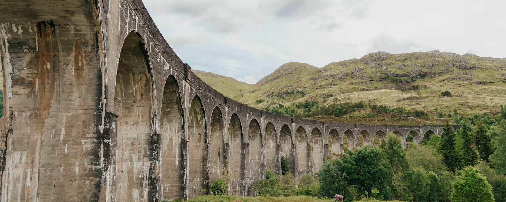 Stone railway viaduct curving past a green hillside and trees