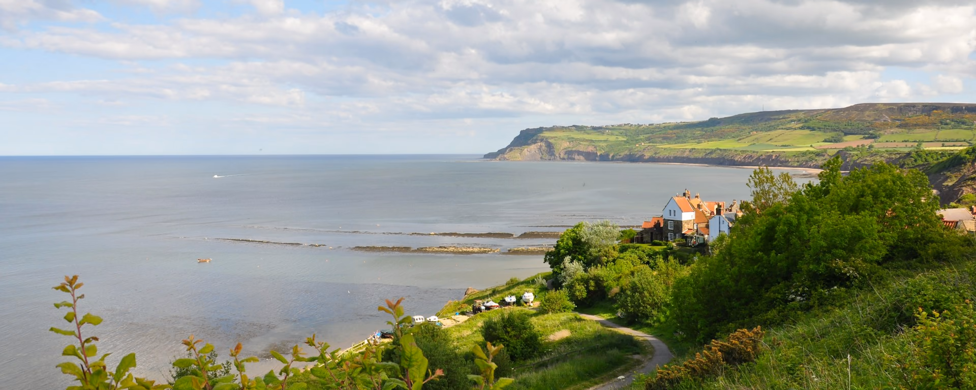 Coastal village and headland from a green clifftop, with the sea beyond