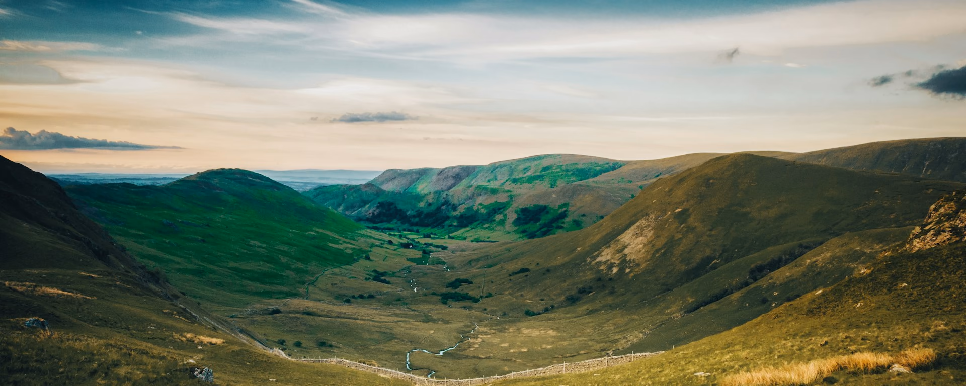 Green valley with a stream and stone wall in the hills under a pale sky