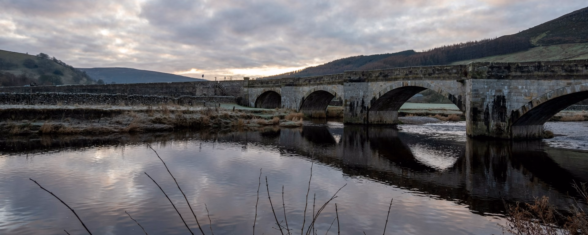 Stone arched bridge over a river at dusk, with its reflection in still water