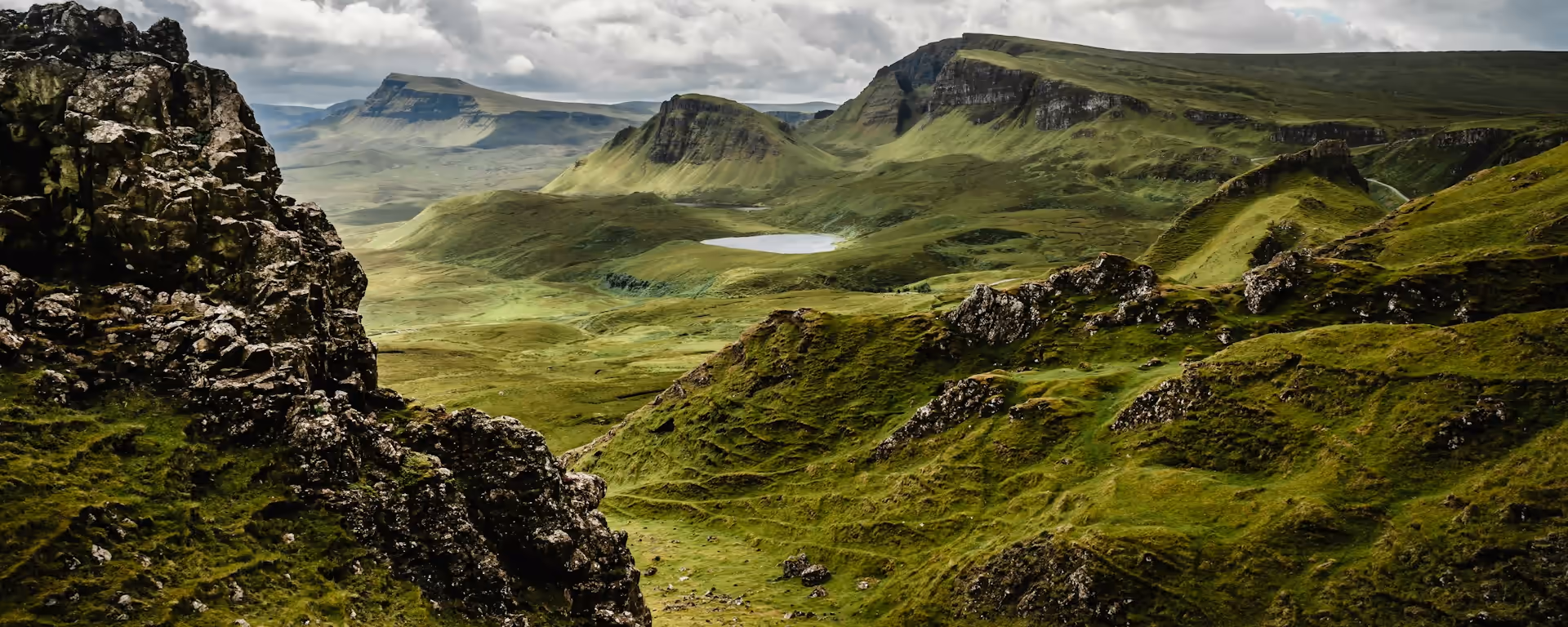 Rocky ridge looking over green table-top hills and a loch under cloud