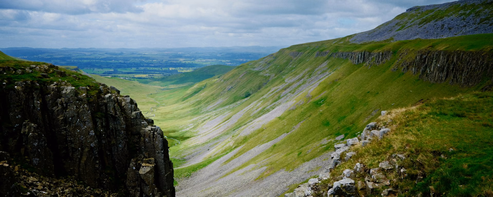 Steep limestone gorge dropping to a green valley under cloud
