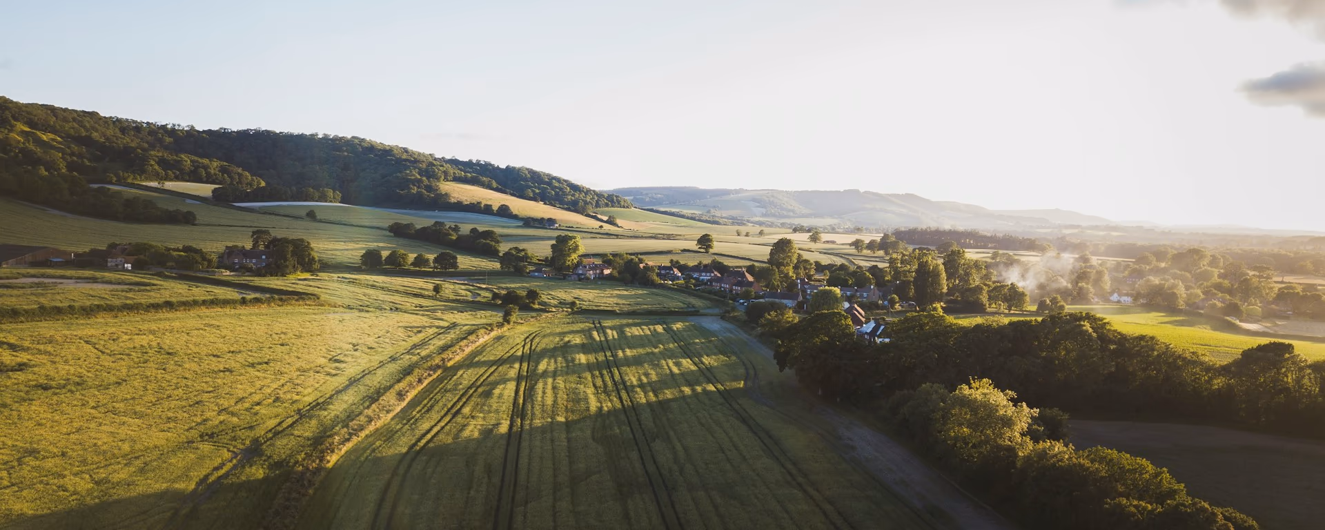 Sunlit fields and a village tucked under a wooded ridge