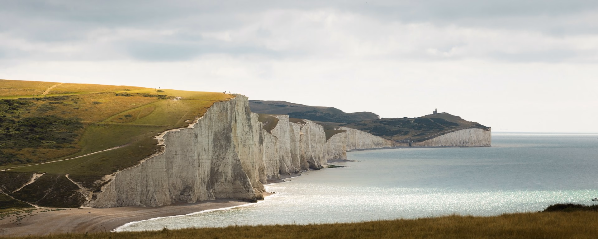 White chalk cliffs and sea seen from a grassy hill under cloud