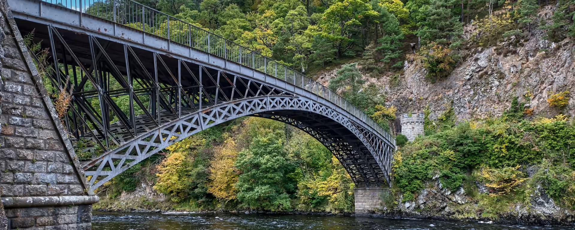 Iron arched bridge over a wooded river, with a stone abutment in the foreground